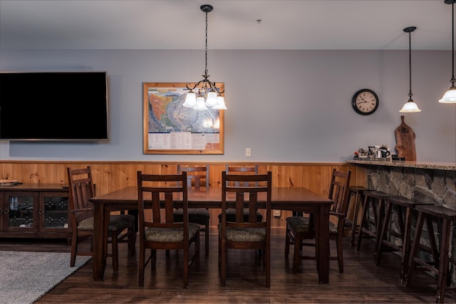 dining room featuring a notable chandelier, wooden walls, dark hardwood / wood-style floors, and indoor bar