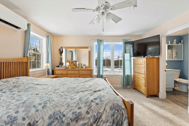 carpeted bedroom featuring ceiling fan, ensuite bathroom, and a wall mounted air conditioner