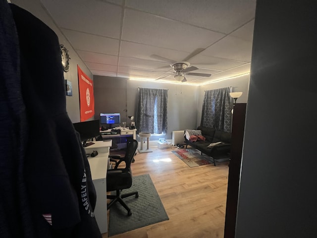 office space with ceiling fan, a paneled ceiling, radiator heating unit, and hardwood / wood-style flooring