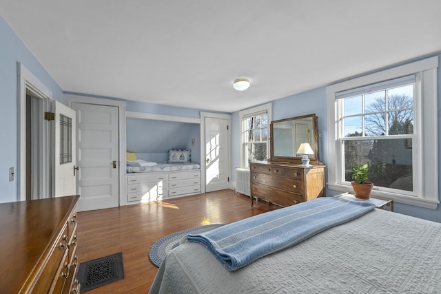 bedroom with multiple windows, radiator heating unit, and dark hardwood / wood-style floors