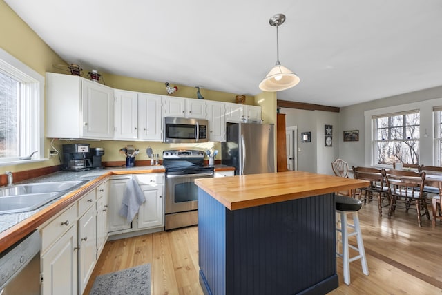 kitchen featuring pendant lighting, a breakfast bar, appliances with stainless steel finishes, butcher block countertops, and white cabinetry