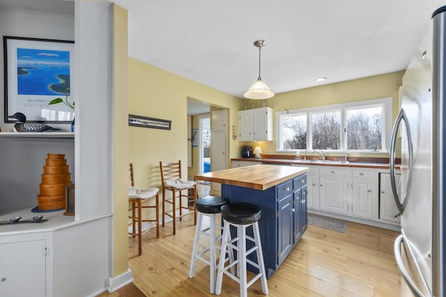 kitchen with wooden counters, a kitchen breakfast bar, blue cabinets, white cabinetry, and stainless steel refrigerator