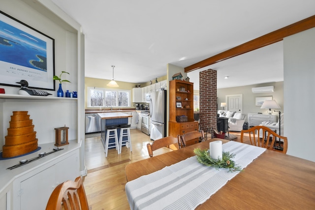 dining area featuring a wall mounted air conditioner, light hardwood / wood-style floors, sink, and beam ceiling