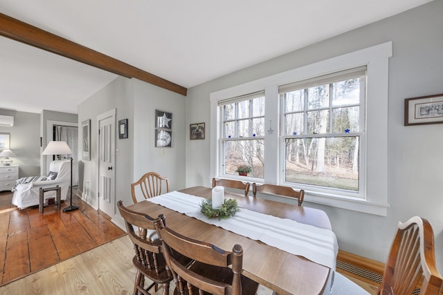 dining space featuring a wall mounted AC, beamed ceiling, and light wood-type flooring