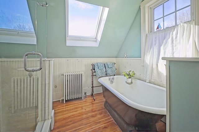 bathroom featuring hardwood / wood-style flooring, lofted ceiling with skylight, radiator, and a bathing tub