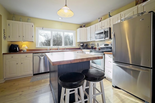 kitchen with butcher block counters, a kitchen breakfast bar, hanging light fixtures, white cabinetry, and stainless steel appliances