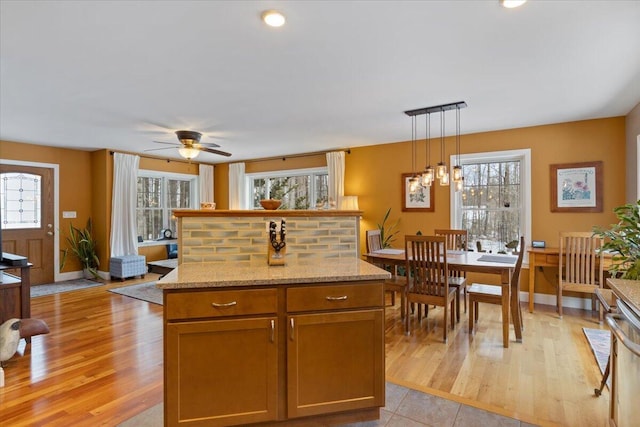 kitchen with decorative light fixtures, light stone counters, a healthy amount of sunlight, and ceiling fan with notable chandelier