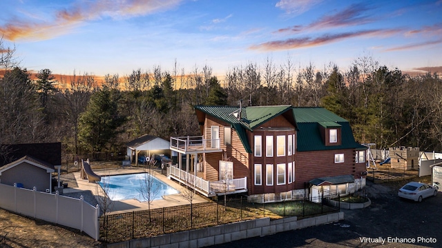 back house at dusk featuring a fenced in pool and a balcony