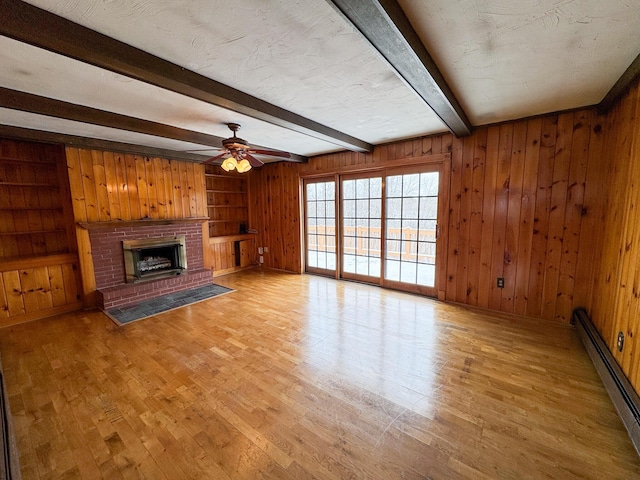 unfurnished living room with a fireplace, a baseboard heating unit, wood walls, and beamed ceiling