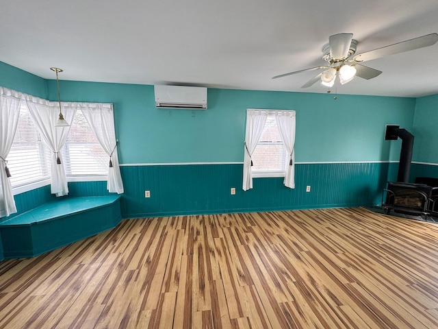 interior space with ceiling fan, a wall mounted air conditioner, a wood stove, and wood-type flooring