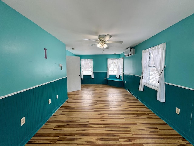 unfurnished room featuring a wall unit AC, hardwood / wood-style floors, and ceiling fan