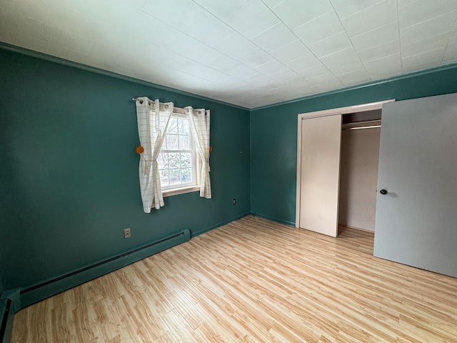 unfurnished bedroom featuring a baseboard heating unit, a closet, and light hardwood / wood-style flooring