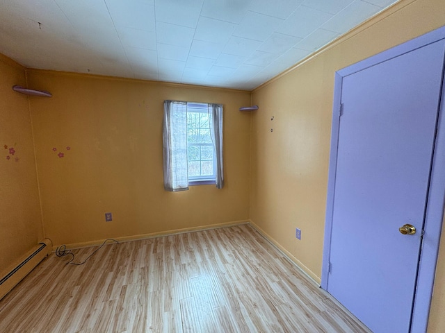 spare room featuring baseboard heating, light hardwood / wood-style flooring, and crown molding