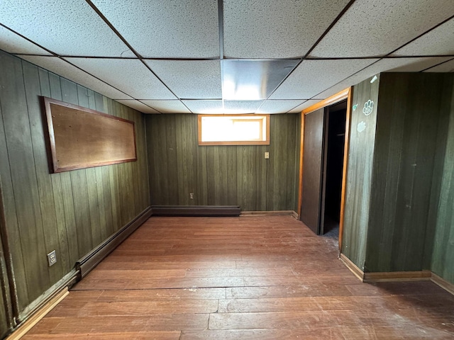 basement featuring a paneled ceiling, hardwood / wood-style floors, and wooden walls