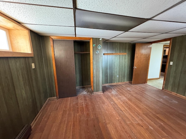 interior space featuring hardwood / wood-style floors, a closet, a paneled ceiling, wooden walls, and a baseboard heating unit