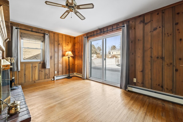 unfurnished living room featuring baseboard heating, ceiling fan, light hardwood / wood-style flooring, and wood walls