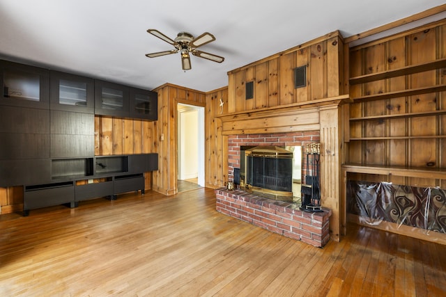 living room featuring a fireplace, light hardwood / wood-style floors, ceiling fan, and wood walls