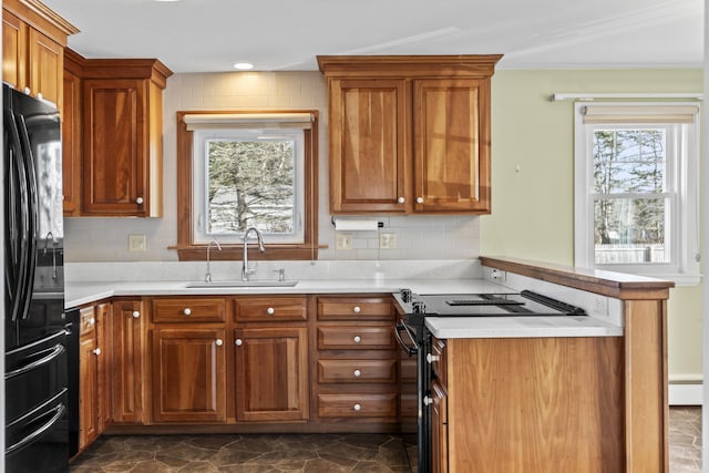 kitchen with black appliances, baseboard heating, sink, and a wealth of natural light