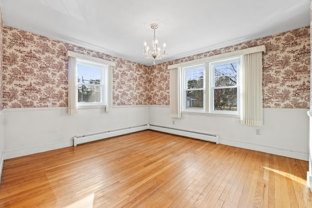 empty room featuring a notable chandelier, wood-type flooring, and a baseboard heating unit