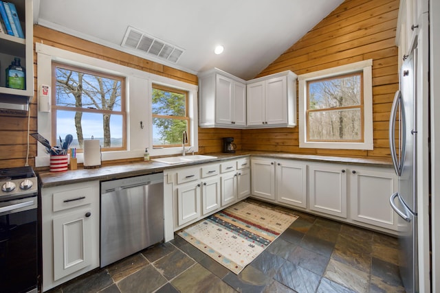 kitchen featuring vaulted ceiling, appliances with stainless steel finishes, wooden walls, sink, and white cabinetry