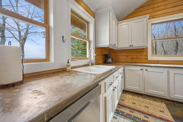 kitchen with sink, wooden walls, white cabinets, dishwasher, and lofted ceiling