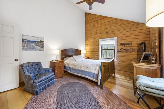 bedroom with light wood-type flooring, ceiling fan, vaulted ceiling, and wooden walls