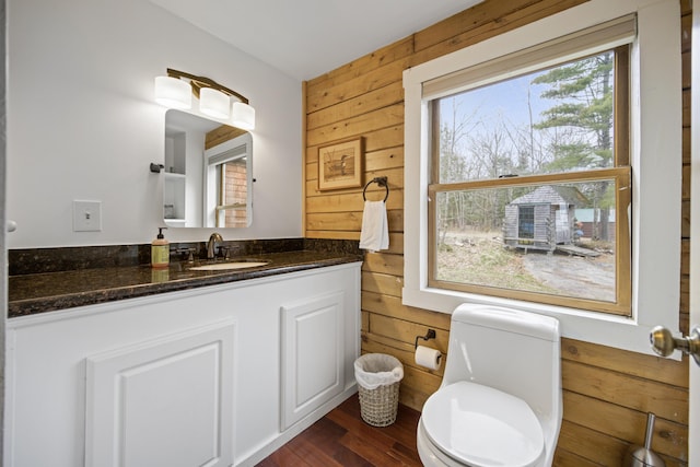 bathroom featuring wood-type flooring, wooden walls, vanity, and toilet