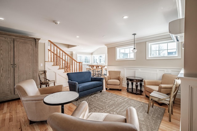 living room featuring lofted ceiling, a wall mounted AC, light hardwood / wood-style flooring, ornamental molding, and radiator heating unit