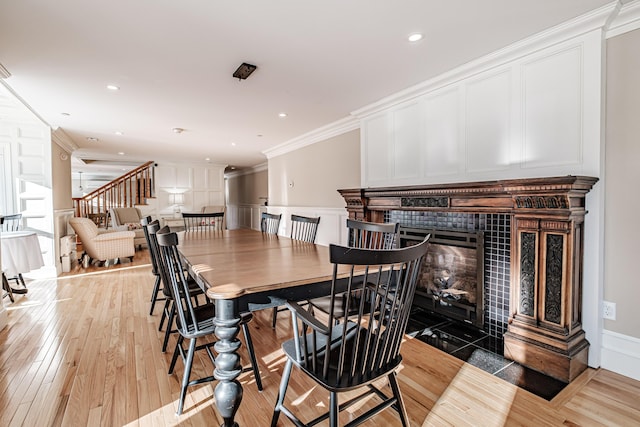 dining space with light wood-type flooring, a tiled fireplace, and ornamental molding