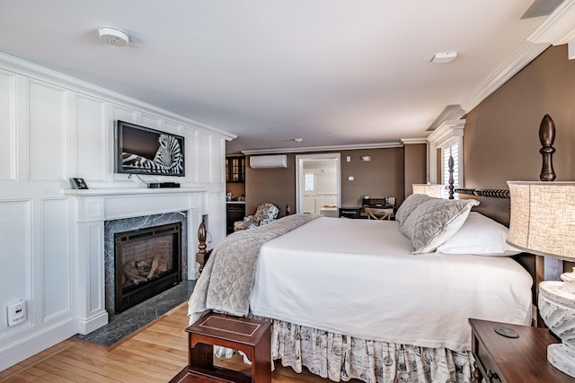 bedroom with an AC wall unit, wood-type flooring, crown molding, and a fireplace