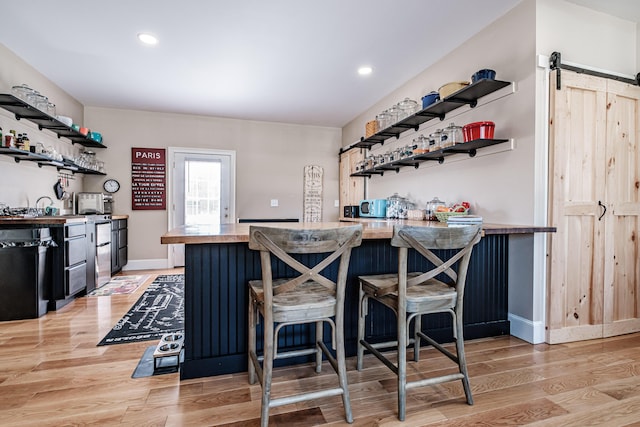 bar with a barn door, black dishwasher, and light hardwood / wood-style floors