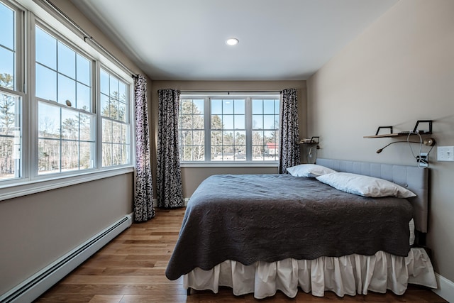 bedroom with a baseboard heating unit and light hardwood / wood-style flooring