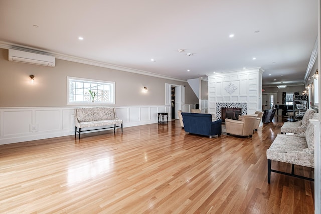 living room featuring ornamental molding, a tile fireplace, a wall unit AC, and light wood-type flooring