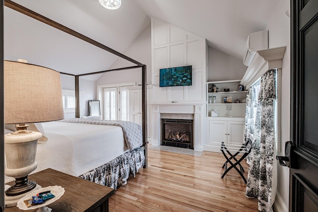 bedroom featuring light wood-type flooring, vaulted ceiling, and a wall mounted air conditioner