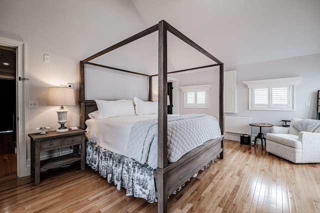 bedroom with light wood-type flooring, vaulted ceiling, and radiator heating unit