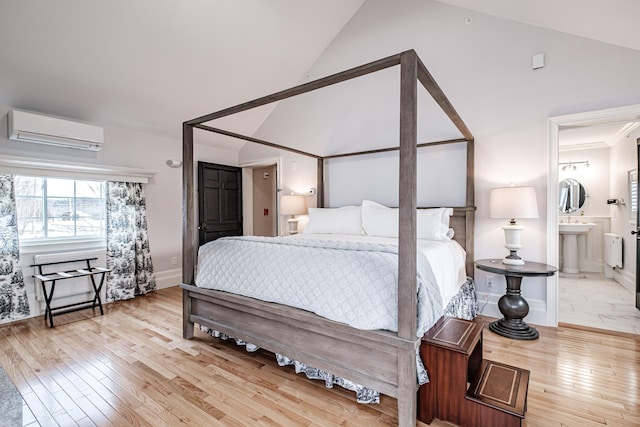 bedroom with a wall unit AC, ensuite bathroom, vaulted ceiling, and light wood-type flooring