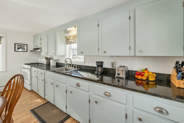 kitchen featuring sink, white gas stove, dark stone counters, and light wood-type flooring