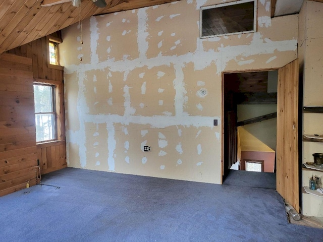 spare room featuring carpet floors, ceiling fan, wooden walls, and high vaulted ceiling