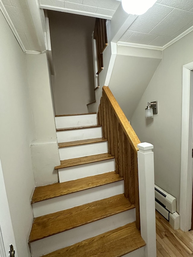 stairway featuring hardwood / wood-style floors, baseboard heating, and crown molding