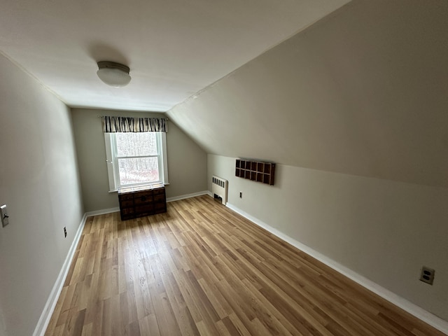 bonus room featuring radiator heating unit, light hardwood / wood-style floors, and lofted ceiling