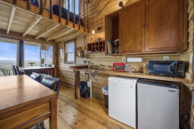 kitchen with wood ceiling, wood walls, stainless steel refrigerator, light hardwood / wood-style floors, and refrigerator