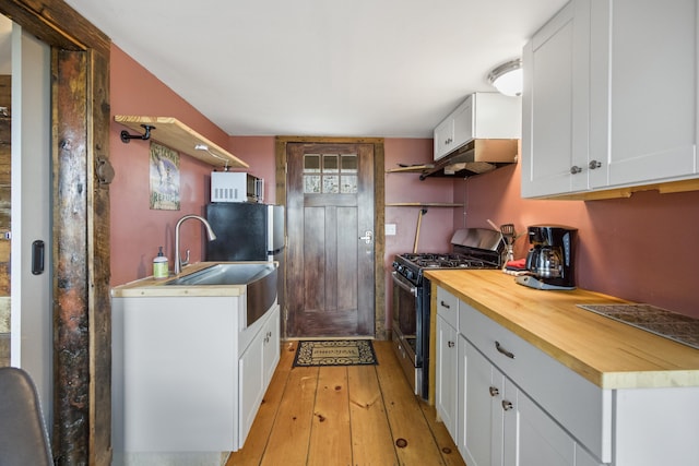 kitchen with light hardwood / wood-style flooring, butcher block countertops, white cabinets, stainless steel range with gas stovetop, and sink