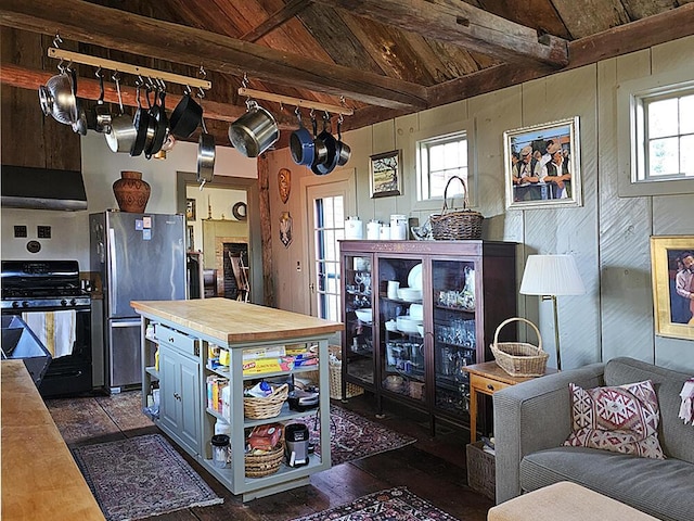 kitchen featuring black gas range oven, wood walls, stainless steel refrigerator, and wood ceiling