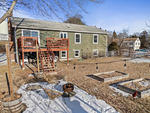 snow covered rear of property with a deck and a fire pit