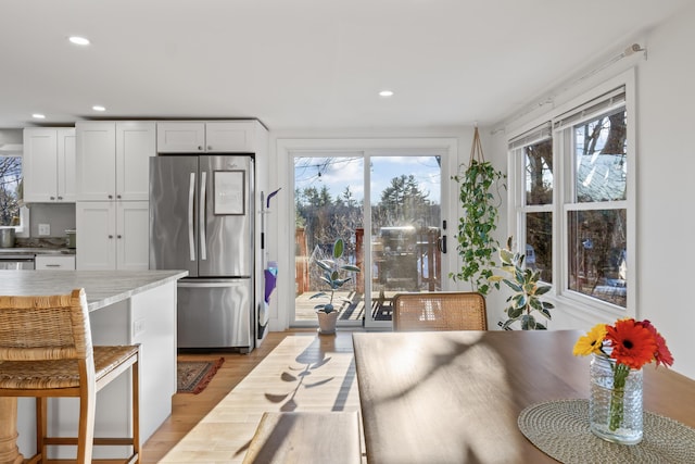 kitchen featuring white cabinetry, light hardwood / wood-style flooring, a breakfast bar, and stainless steel refrigerator