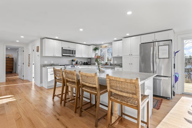 kitchen featuring a kitchen bar, stainless steel appliances, light wood-type flooring, white cabinets, and a center island