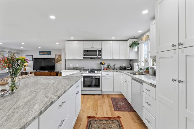 kitchen with appliances with stainless steel finishes, white cabinetry, sink, light stone counters, and light hardwood / wood-style flooring