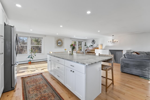 kitchen featuring a center island, a breakfast bar, white cabinets, stainless steel fridge, and light stone counters