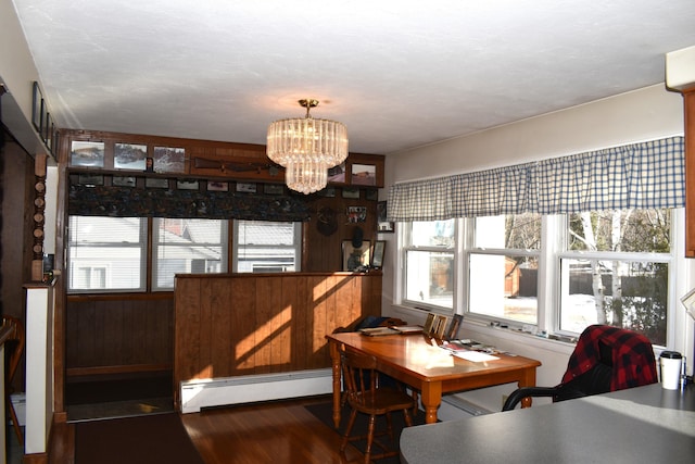 dining area featuring a chandelier, wood walls, dark wood-type flooring, and a baseboard heating unit