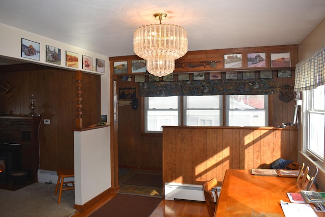 dining space featuring a baseboard heating unit, wood-type flooring, an inviting chandelier, a fireplace, and wood walls